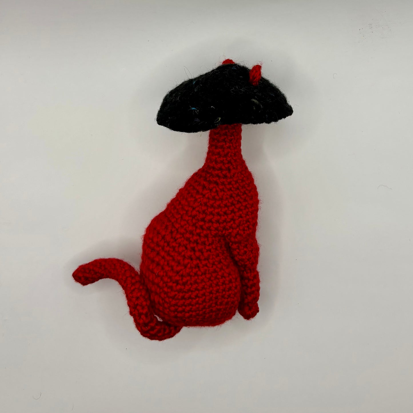 Red crocheted cat with a black mushroom cap for a head on a white background