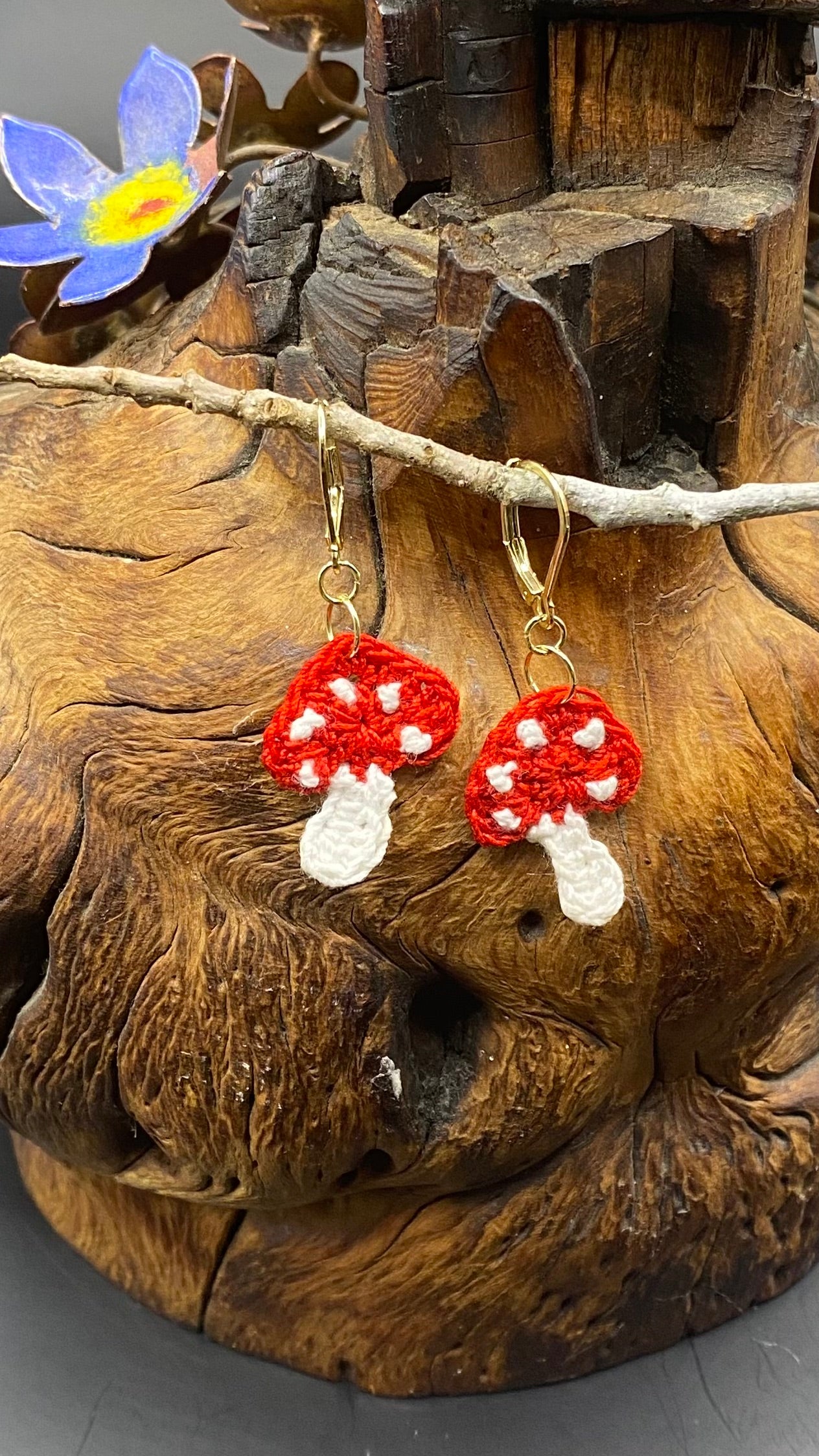 Red and white mushroom earrings on a wooden surface with a decorative flower.