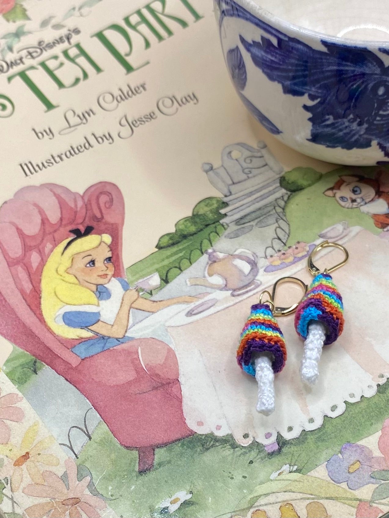 Two colorful mushroom earrings on a book surface featuring an illustration of a character in a chair.