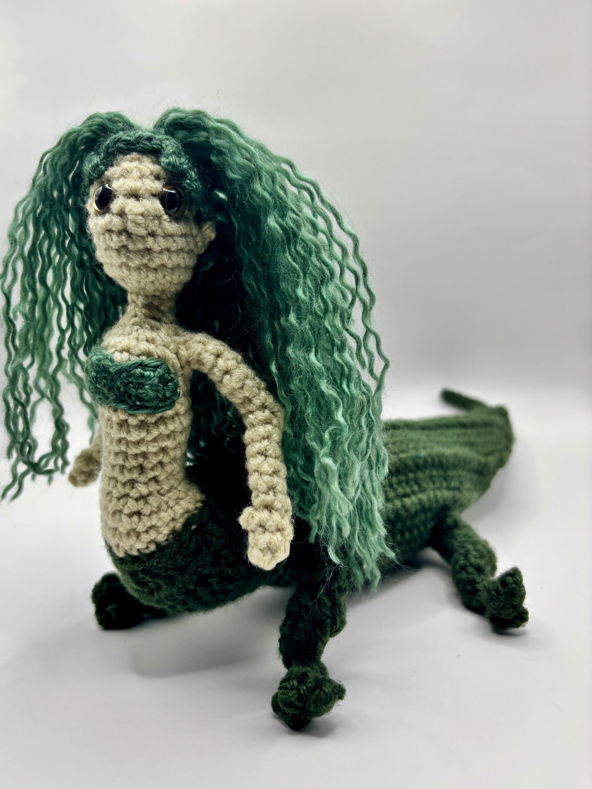 Crocheted mergator sculpture with green hair on a white background