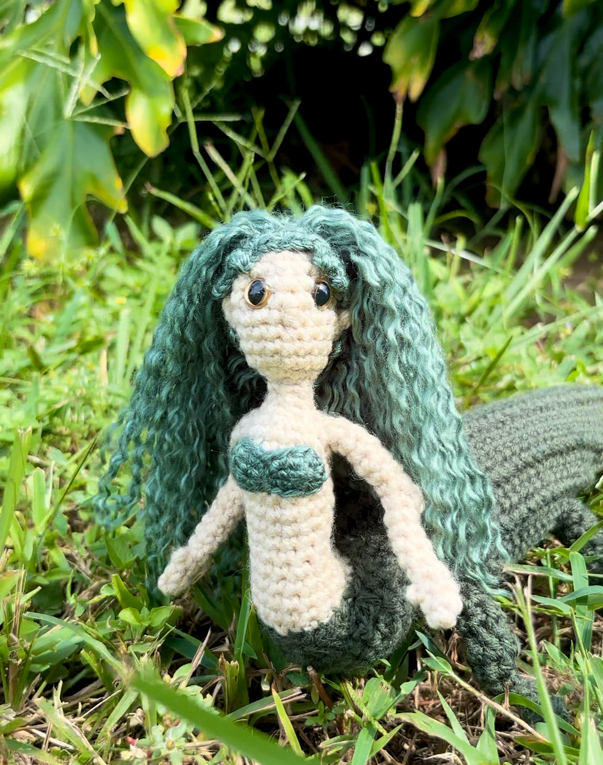 Crocheted mergator with green hair and tail on grass