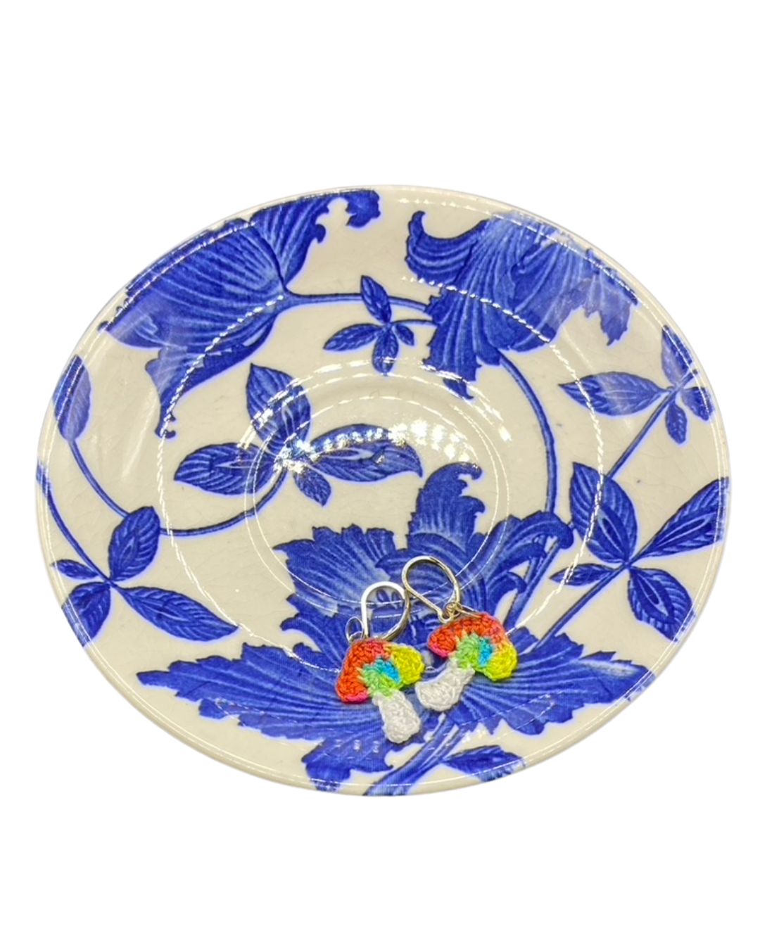 colorful mushroom earrings on a decorative plate with blue floral pattern on a white background
